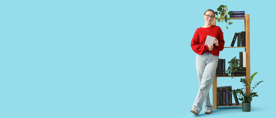 Beautiful young woman with book near bookshelf on blue background