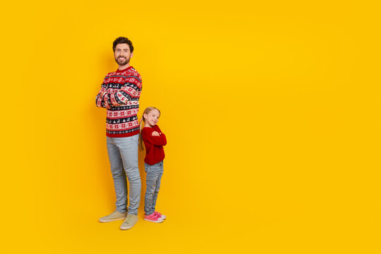 Single father and daughter standing against a yellow background in festive sweaters, expressing joy