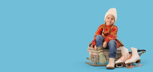 Cute little girl in winter clothes putting warm sock on her foot against blue background with space for text