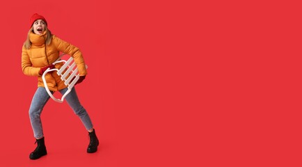 Going young woman in warm winter clothes and with sledge on red background with space for text