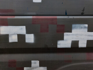 Abstract industrial camouflage pattern on dark metal, featuring pixelated white and faded red blocks, creating a modern, urban grunge texture with subtle reflections.