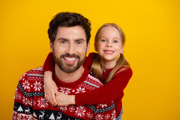 Happy father and daughter smiling together in festive Christmas sweaters against a bright yellow...