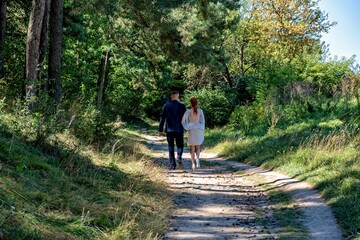 A man and woman walking hand in hand down a dirt path in a wooded area