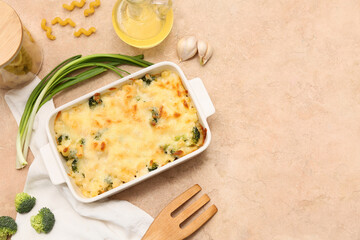 Baking dish with tasty pasta, broccoli, garlic and green onion on beige grunge background