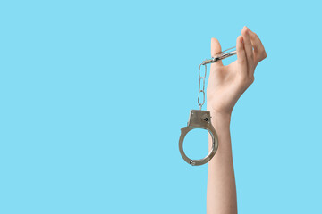 Female hand with handcuffs on blue background