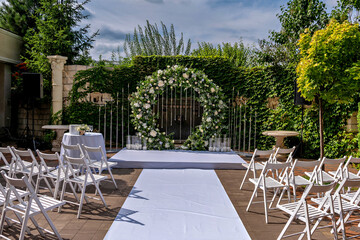 A white aisle runner leads to a white archway with white flowers surrounded by white chairs and a white table