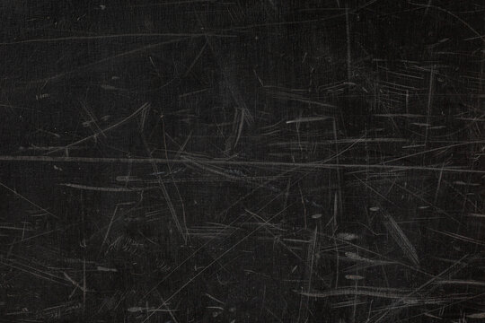 Dark, heavily scratched surface, worn chalkboard or a painted metal sheet, covered with a dense, chaotic pattern of thin, light-colored scuff marks and abrasions, gritty, textured, grunge abstract bac