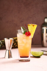 Glass of tasty Mai Tai cocktail garnished with cherry and pineapple on pink background