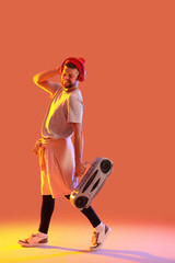 Handsome male hip-hop dancer in headphones with tape-recorder on orange background