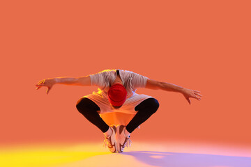 Young man dancing hip-hop on orange background