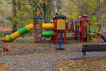 Children’s playground in autumn park with colorful trees and fallen leaves