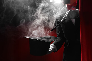 Male magician with hat and wand making smoke behind red curtains
