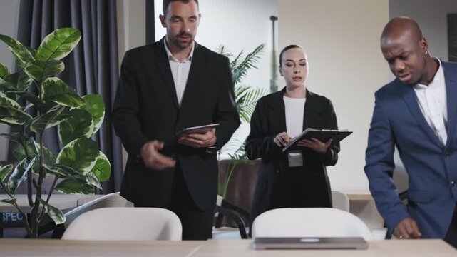 Group of three professionals, two men and one woman, collaborating around a laptop in a modern office, discussing ideas and strategies for business success and teamwork	