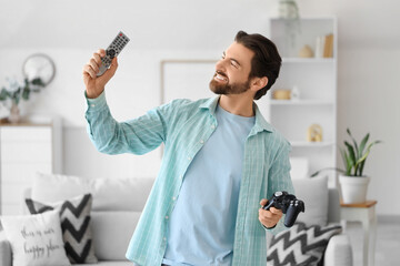 Young man with TV remote controller and game pad at home