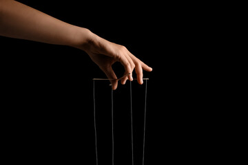 Female hand of puppeteer with strings on black background