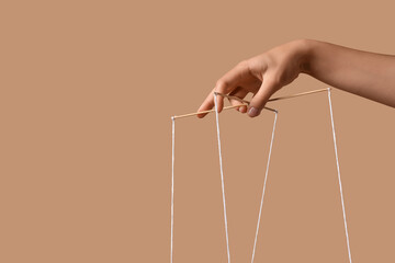 Female hand of puppeteer with strings on beige background
