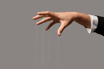 Female hand of puppeteer with strings on grey background