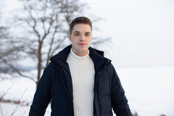 Portrait of young handsome man in sweater and coat in winter park