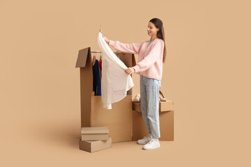 Young woman with dress and wardrobe boxes on beige background