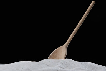Wooden spoon scooping or mixing natural granulated sugar during cooking and baking with black...