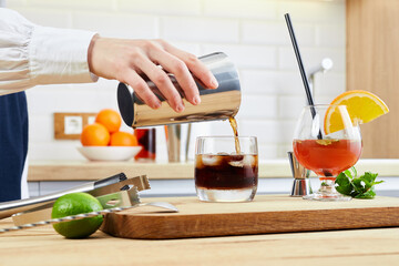 A woman pours an alcoholic drink into a cocktail glass. The concept of cooking, drinks, house parties, mixing spirits.