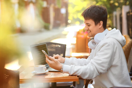Handsome programmer working with laptop and mobile phone at table in street cafe