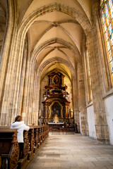 Fototapeta premium Mujer devota rezando de rodillas en la Catedral de Santa Bárbara, en la ciudad de Kutná Hora