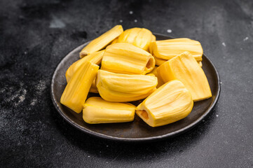 Sweet, golden yellow jackfruit pods (bulbs) served in a black plate on a dark stone background. Exotic tropical fruit with copy space
