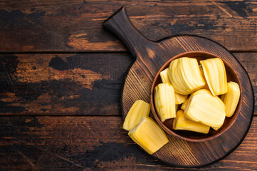 Sweet, golden jackfruit pods (bulbs) in a wooden bowl on a rustic dark wood table. Tropical fruit snack with copy space. © Mironov