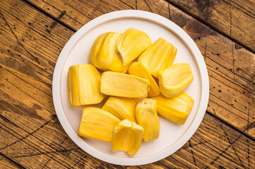 Sweet, golden yellow jackfruit pods (bulbs) served on a white plate on a rustic wooden table. Fresh, tropical fruit snack.