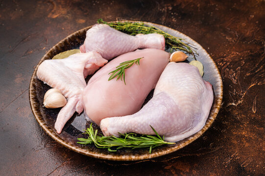 The promise of a perfect roast: prime raw poultry cuts rest with fragrant rosemary, thyme, and garlic on a deep, earthen plate, awaiting their culinary transformation.