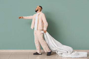 Male sleepwalker in pajamas with blanket near green wall