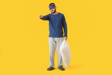 Male sleepwalker in pajamas with pillow on yellow background