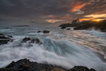 Dramatic long exposure of waves crashing on the rocky coast near the Santa Catalina hermitage in Mundaka, Bizkaia, Basque Country, under a vibrant sunset sky