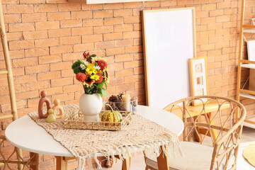Vase with autumn flowers and pumpkins on dining table in room