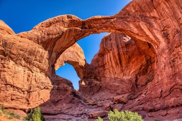 Arches Nationalpark, Moab in Utah US.. sunlit red rock desert landscape reveals towering sandstone spires and eroded fins under clear azure sky.