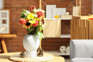 Vase with autumn flowers and fir cones on table in living room