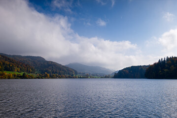Lake landscape with autumn trees and cloudy sky. Fall season, serene nature. Peaceful lake and colorful forest scenery. T&uuml;rlersee, Switzerland.