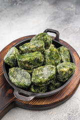 Overhead shot of frozen spinach blocks in a cast iron skillet on a wooden board. Grey textured background with copy space.