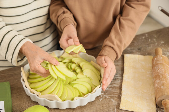 Senior woman with her grandson making apple pie in kitchen, closeup