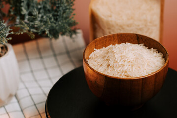Long grain white rice in a wooden bowl on a black plate with greenery in the background