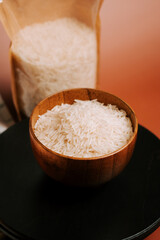 Freshly harvested long grain white rice in a wooden bowl with a pack in the background