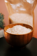 Bowl of long grain white rice next to package on a wooden surface