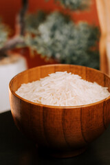 Long grain white rice in a wooden bowl with green plants in the background