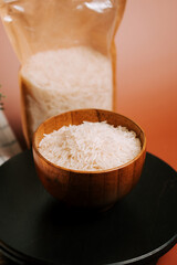 Long grain white rice in a wooden bowl with a background of rice package