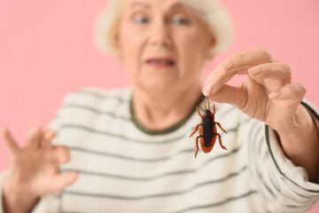 Scared senior woman with cockroach on pink background, closeup