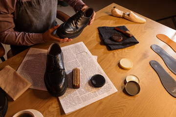 Male shoemaker polishing shoes at table in dark workshop