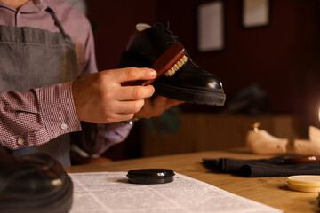 Male shoemaker polishing shoes with brush at table in dark workshop, closeup