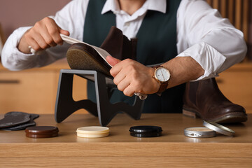 Male shoemaker polishing leather boot at table in workshop