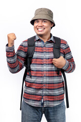A man smiles wearing a travel look, with a bucket hat, flannel shirt, jeans, and black bag with a white background.